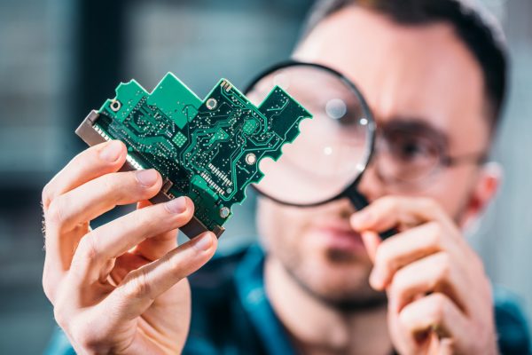 Close-up view of man looking at circuit board through magnifying glass